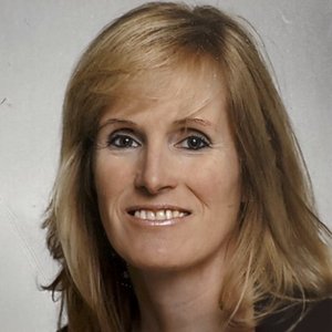 Eine blonde Frau blickt freundlich lächelnd in die Kamera